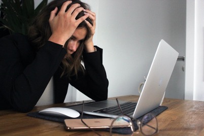 Woman looking down at her laptop with her head in her hands